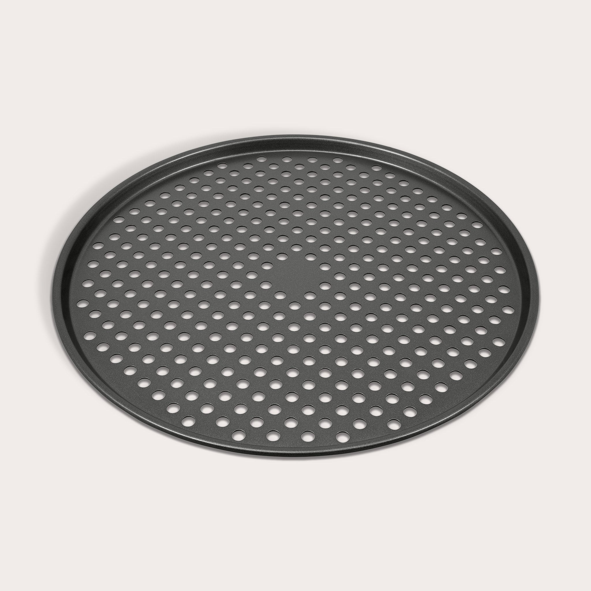 The Zyliss Non-Stick Pizza Tray is a round, black, carbon steel tray featuring numerous evenly spaced holes for crispy pizza bases. Shown on a white background.