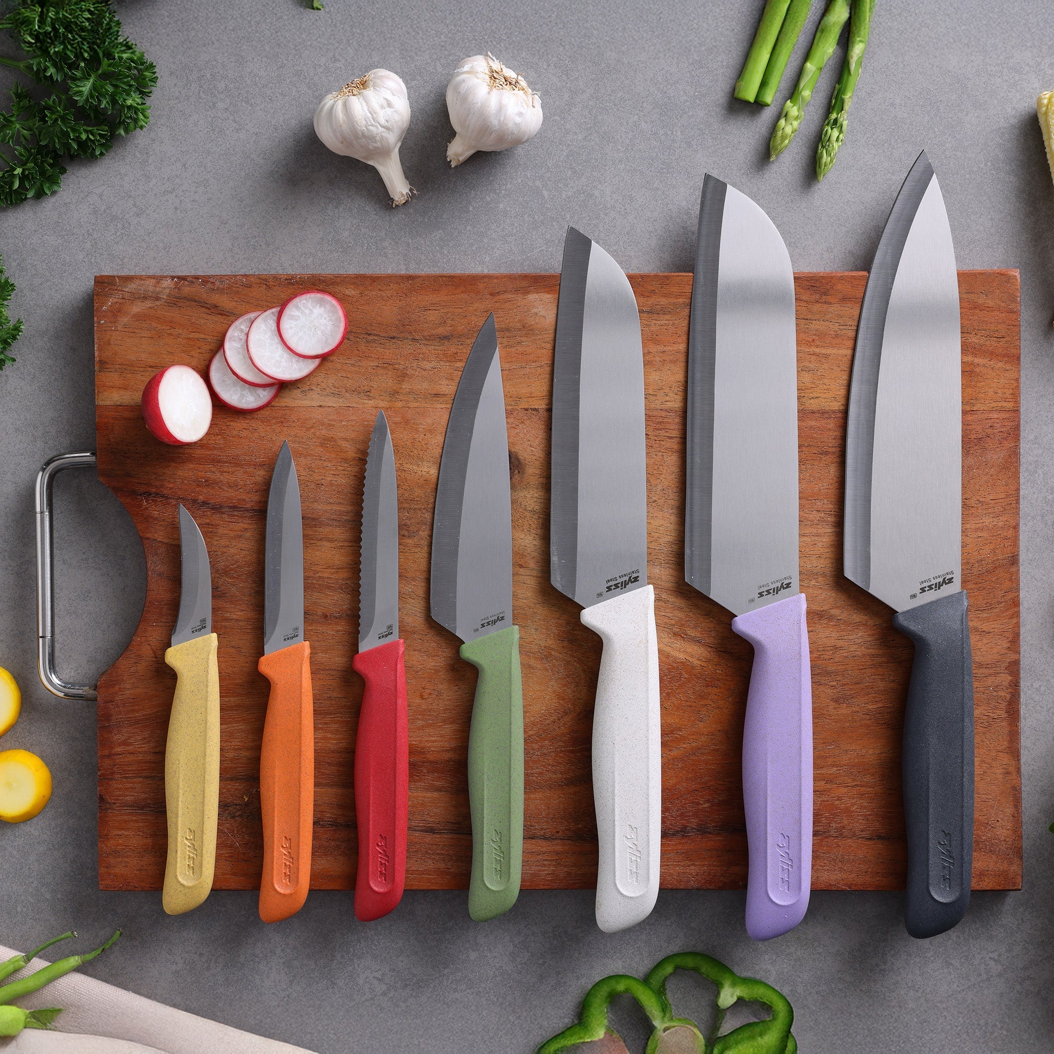 A chef’s knife with a purple handle and matching sheath lies on a white surface, next to sliced purple cabbage on a wooden cutting board.