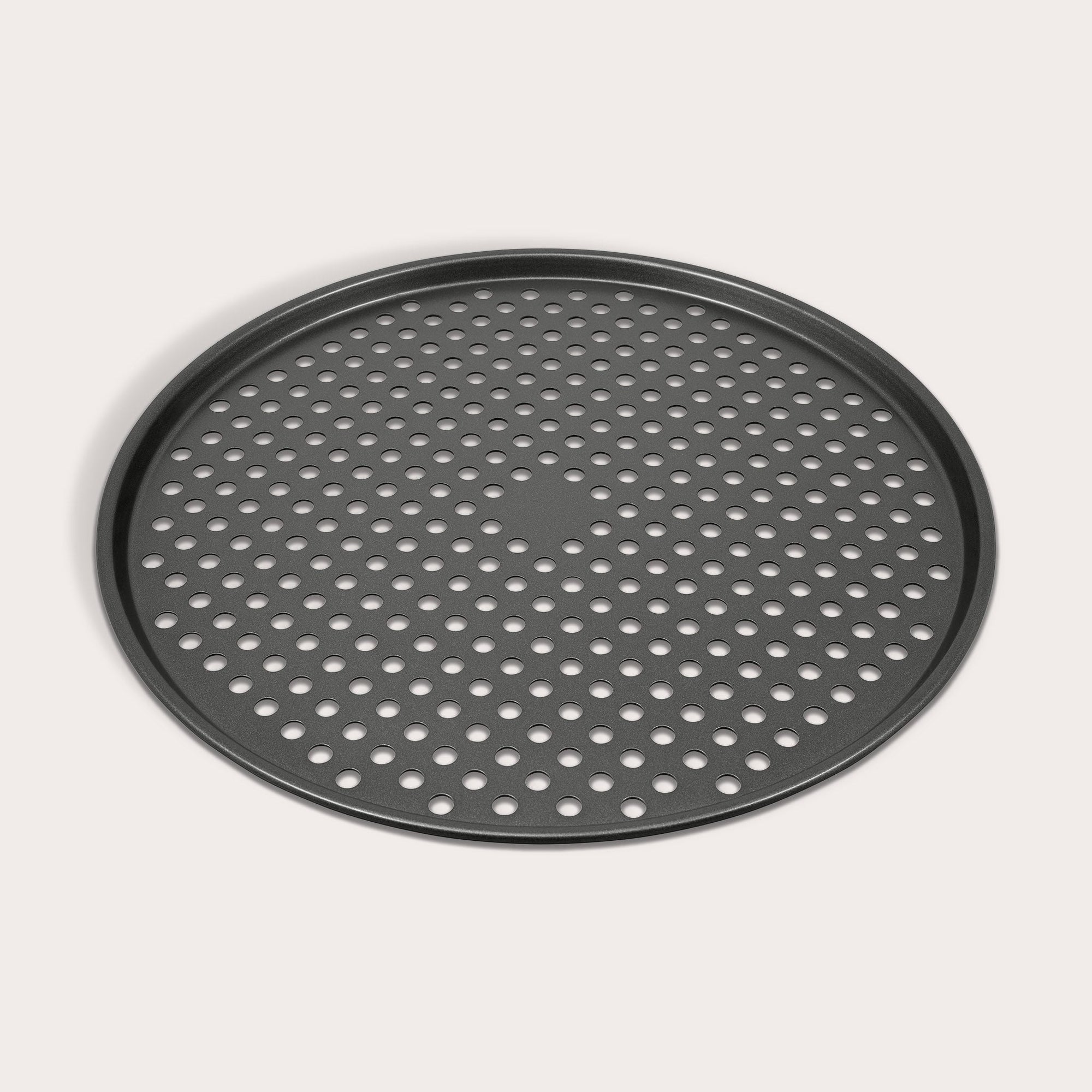 The Zyliss Non-Stick Pizza Tray is a round, black, carbon steel tray featuring numerous evenly spaced holes for crispy pizza bases. Shown on a white background.