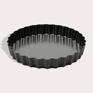 The Zyliss Non-Stick Tart Pan is round and black with fluted edges, a flat bottom, and a removable base—ideal for baking tarts or quiches. The empty pan is displayed on a light background.