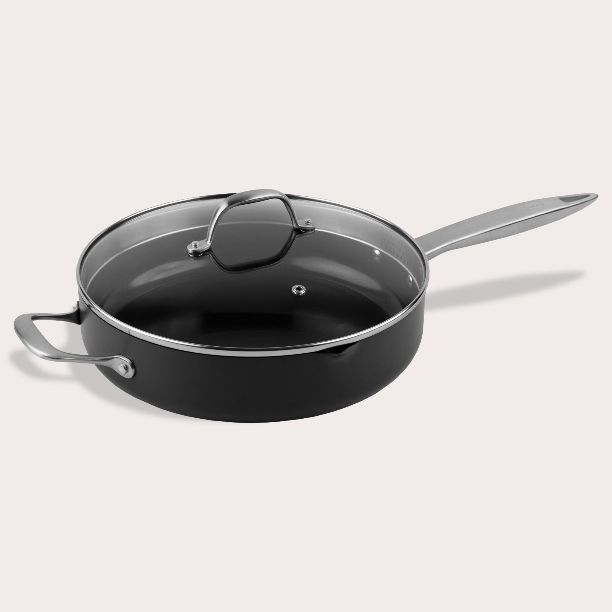 A Zyliss Ultimate Pro Ceramic Saute Pan With Lid, featuring a black nonstick surface, glass lid, long metal handle, and short helper handle, is displayed against a plain light background. 