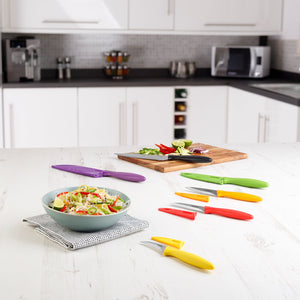 A modern kitchen features the Zyliss 6 Piece Knife Set with matching sheaths on a white countertop, alongside a bowl of salad and cut vegetables on a chopping board—ideal for efficient food preparation. 