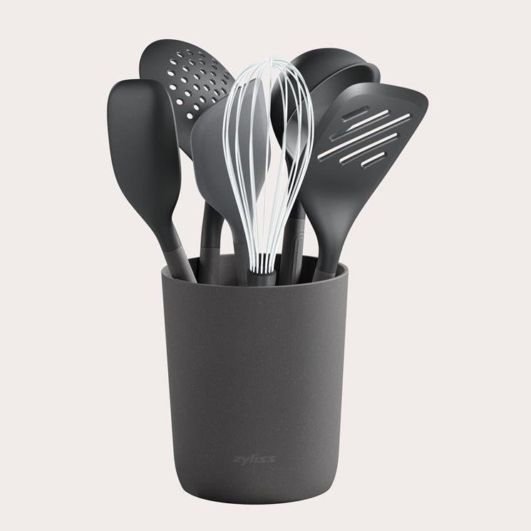 A set of black kitchen utensils, including spatulas, a spoon, a slotted spoon, and a whisk, neatly arranged in a matching black holder against a plain background.