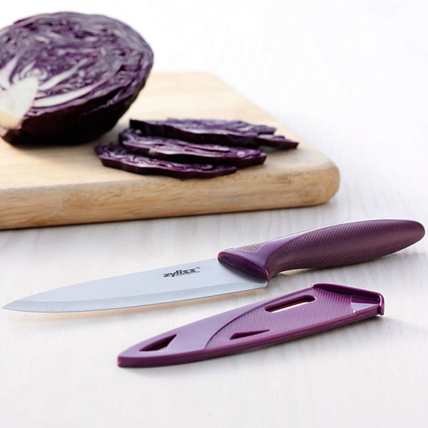 A Zyliss 3 Piece Knife Set chef’s knife with a purple handle rests on a light wooden surface beside slices of red cabbage, highlighting one of the most versatile and essential kitchen tools. 