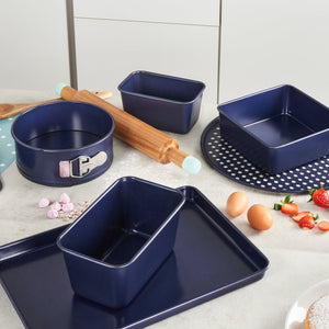 A kitchen countertop features the Zyliss Durable Non-Stick Oven Tray, navy blue baking pans, a rolling pin with teal handles, eggs, and strawberries—perfect for even heat distribution while baking. #23cm/9"