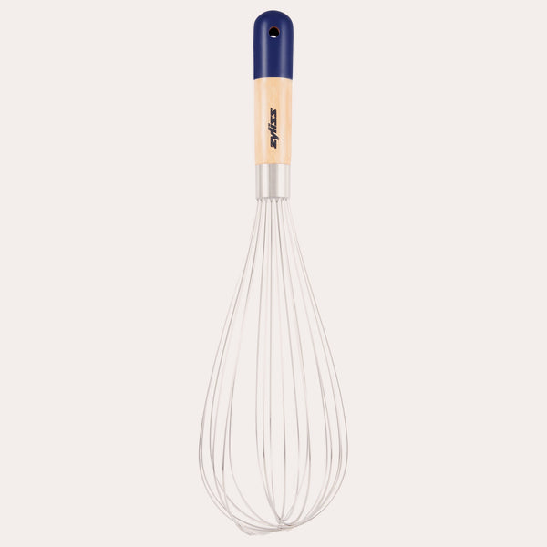 The Zyliss Beech Wood Balloon Whisk has stainless steel wires, a beech wood handle with a blue tip, small hanging hole, and printed logo. Shown on a plain white background. 