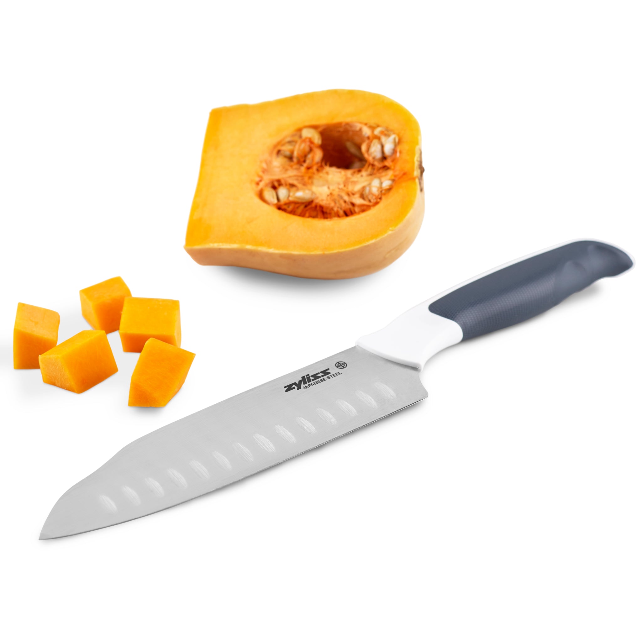 The Zyliss Comfort Santoku Knife 18cm/7, with a black and white handle and Granton-edged blade, lies next to a halved pumpkin and diced cubes on a white background, highlighting its elegant Japanese-inspired design.