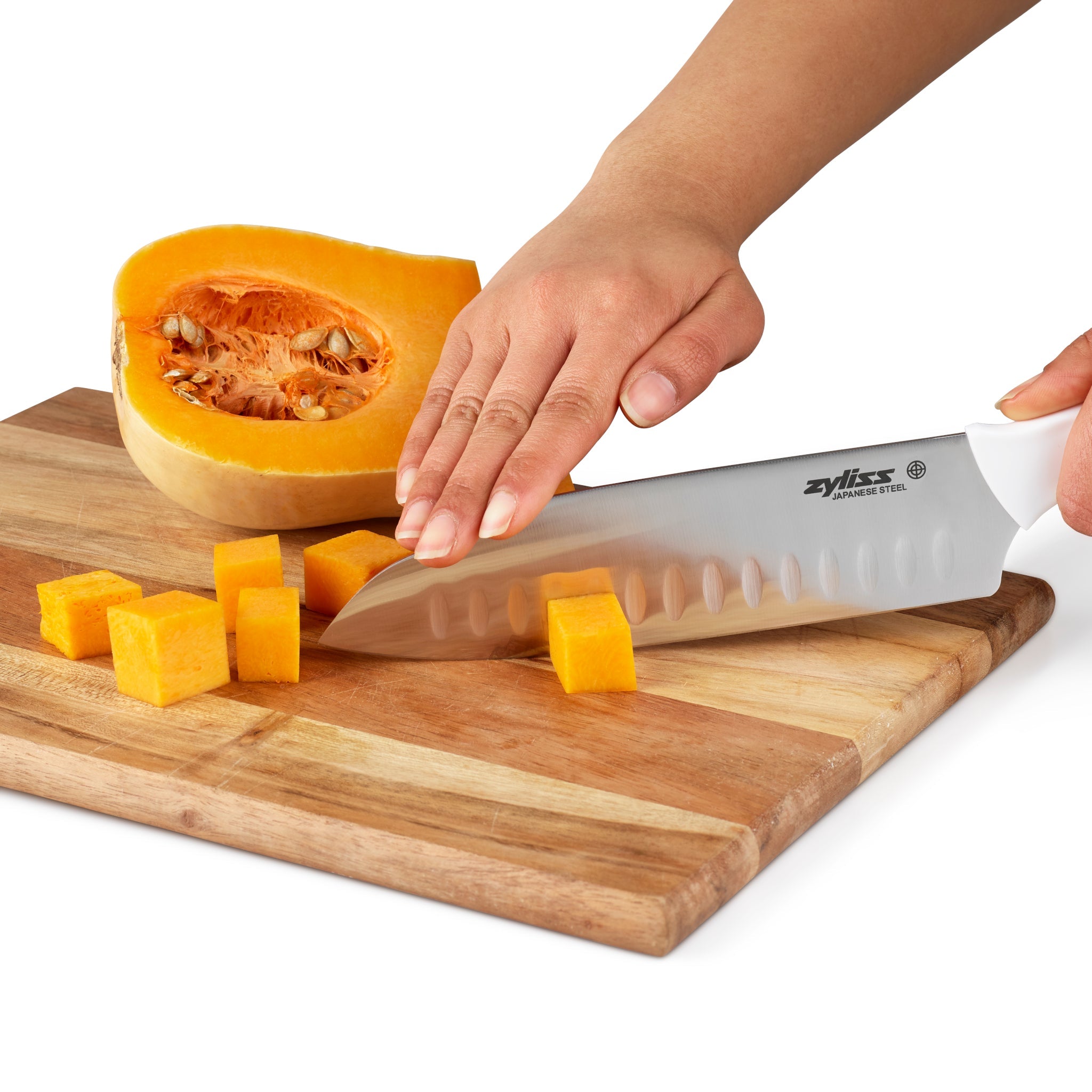 A person’s hand slicing a butternut squash into cubes on a wooden cutting board using a stainless steel chef’s knife. Half of the squash is placed beside the cutting area.