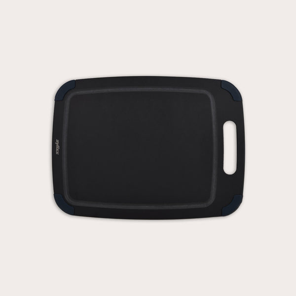 The Zyliss Wood Fibre Cutting Board is a rectangular, black, eco-friendly board with rounded corners, groove edging, right-side handle cutout, and dark blue corner accents. Made from recycled wood fibres. Shown on a plain white background. #Medium