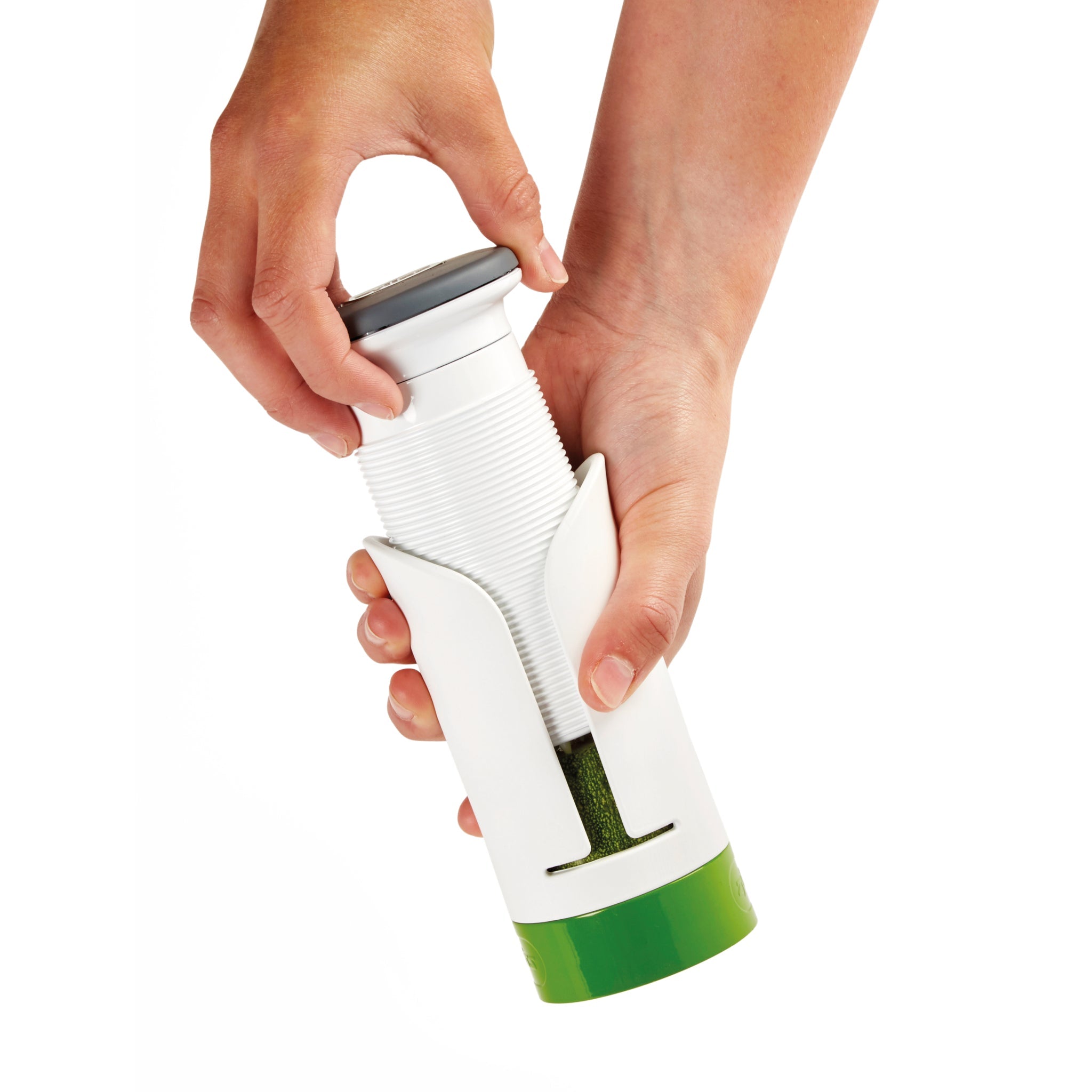 A person’s hands using a white and green spiralizer to cut a zucchini into spiral-shaped pieces.