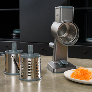 #drumgraterset The Zyliss Gourmet Drum Grater with two interchangeable drums sits on a kitchen counter, with shredded carrots on a white plate nearby and kitchen cabinets in the background.