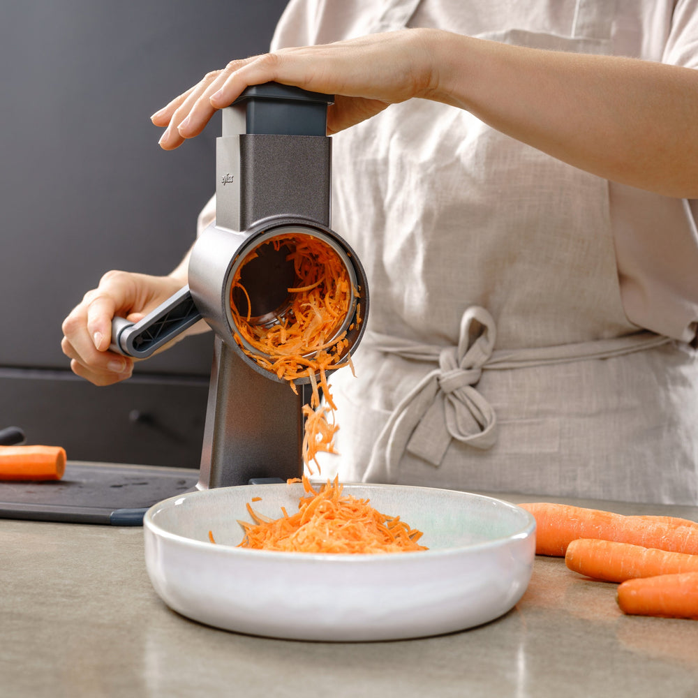 The Zyliss Julienne Drum Gourmet is a metal cylindrical tool with sharp stainless steel blades and a plastic gear attachment, shown against a plain light background. 