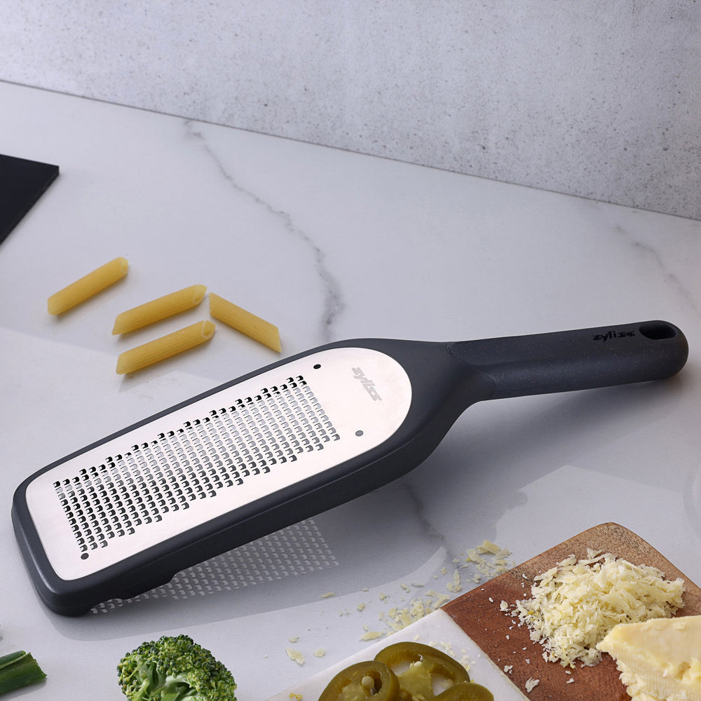 The Zyliss Fine Grater features a black and silver design with a rectangular ultra-sharp grating surface and a handle with an end hole, displayed on a plain light background. 