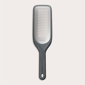 The Zyliss Fine Grater features a black and silver design with a rectangular ultra-sharp grating surface and a handle with an end hole, displayed on a plain light background. 