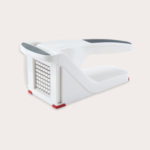 The Zyliss Potato & Vegetable Chipper is a white and gray handheld tool with sharp stainless steel blades, designed to easily slice or dice potatoes and other foods; shown here on a neutral background. 