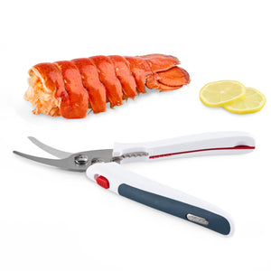 A lobster tail and two lemon slices rest on a white surface next to Zyliss Shellfish Shears, which have curved stainless steel blades and non-slip handles in white, red, and black. 