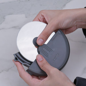 A person holds a Zyliss Pizza Wheel with an ergonomic handle over a marble surface, securing both the pizza and the tool for effortless slicing.