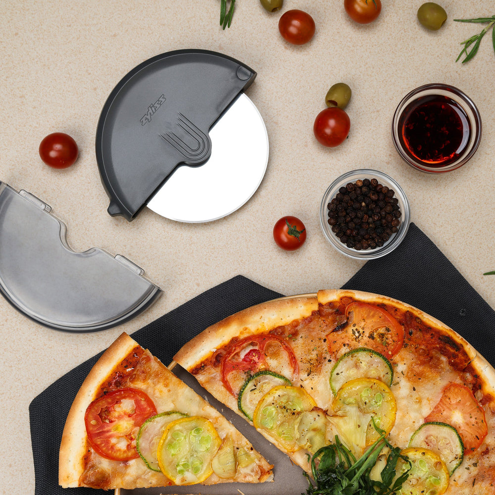 The Zyliss Pizza Wheel sits against a plain light background in a round black and transparent plastic case with a partially open sliding cover, revealing its ergonomic handle and stainless steel blade inside.