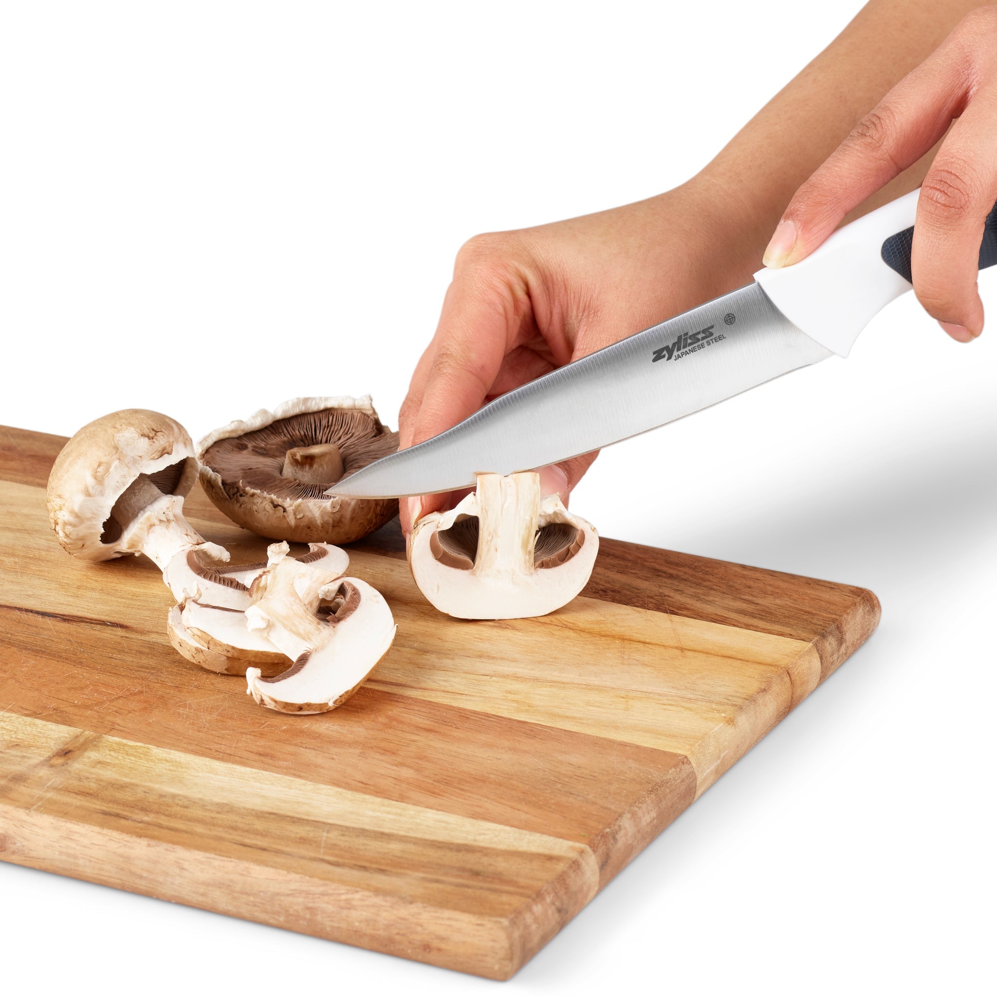 A person slices mushrooms on a wooden cutting board with a large kitchen knife, holding a mushroom in one hand and cutting through it with the other.