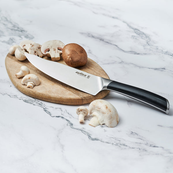The Zyliss Comfort Pro Chefs Knife 20cm / 8 with an ergonomic handle rests on a wooden cutting board, surrounded by sliced and whole mushrooms on a marble countertop. 