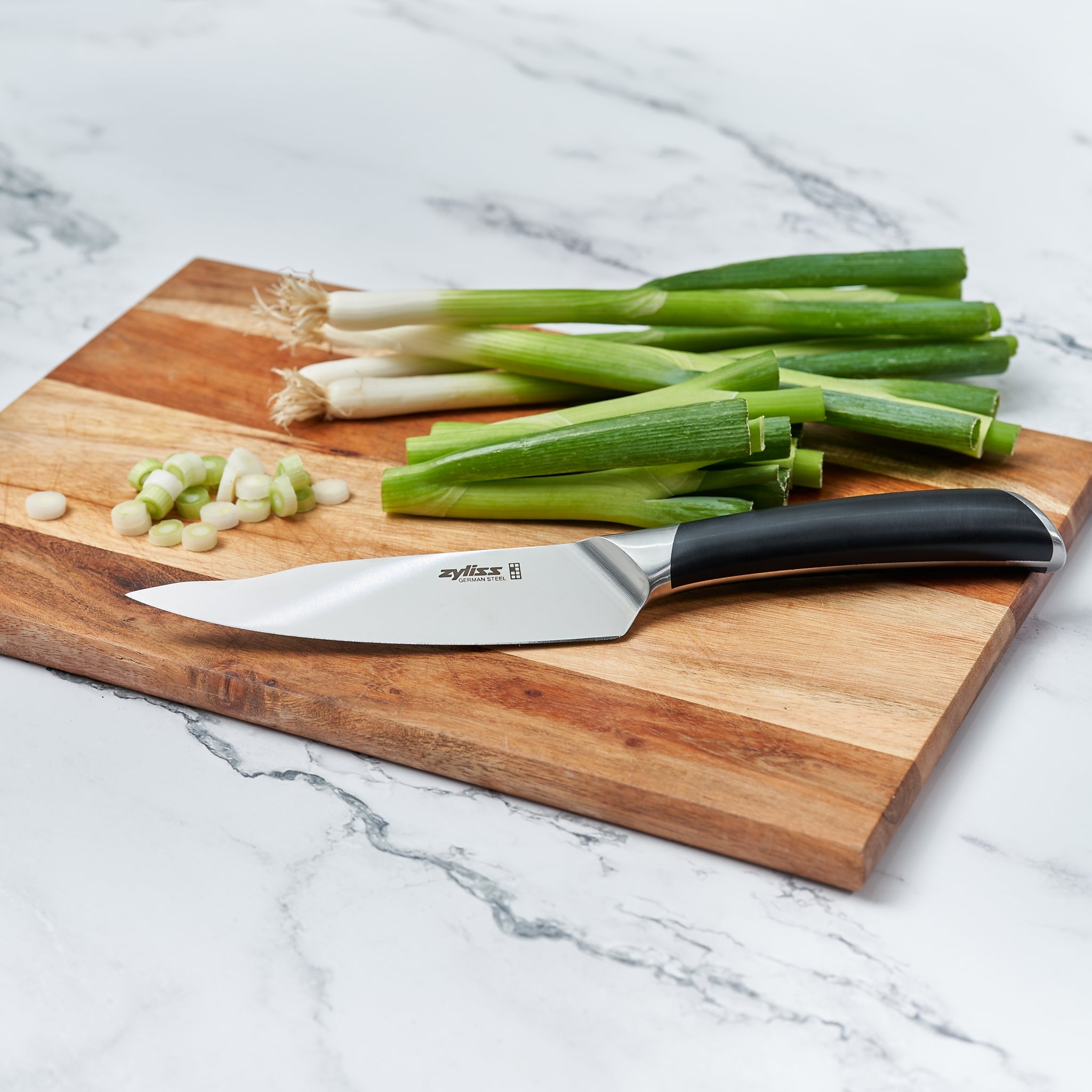 A Zyliss Comfort Pro Utility Knife 14cm/5½ with an ergonomic handle and chopped green onions rest on a wooden cutting board atop a white marble countertop.