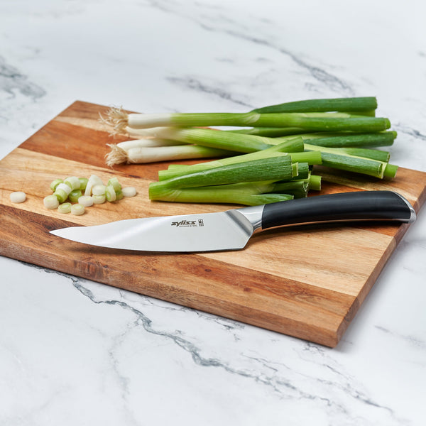 A Zyliss Comfort Pro Utility Knife 14cm/5½ with an ergonomic handle and chopped green onions rest on a wooden cutting board atop a white marble countertop. 