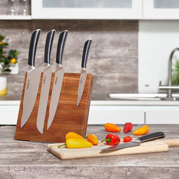 The Zyliss Comfort Pro Magnetic Knife Block, holding four knives, sits on the counter. Nearby, a cutting board displays a knife and sliced mini peppers, with a kitchen sink and other kitchenware in the background. 