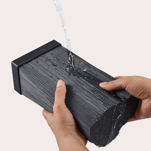 Two hands hold a black rectangular Zyliss Universal Knife Block while water is poured onto it to demonstrate rinsing or cleaning. The background is plain and light-colored.