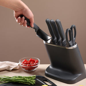 A hand pulls a knife from the Zyliss 8-Piece Knife Block, which holds other knives and scissors. In the background, a bowl of cherry tomatoes and green beans sits on a cutting board.