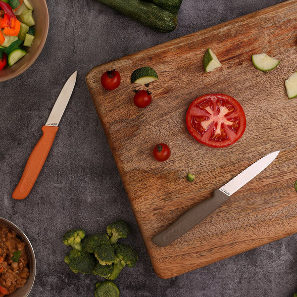 A dark countertop displays the Zyliss 2 Piece Knife Set with a wooden cutting board, sliced tomato, cherry tomatoes, zucchini pieces, broccoli florets, and bowls of chopped vegetables.