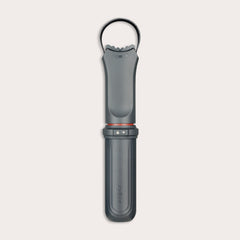 The Zyliss Jar Opener, shown vertically against a light background, is a black and gray handheld tool with a textured grip, integrated locking mechanism, circular top loop, and comes with a protective blade sheath. 