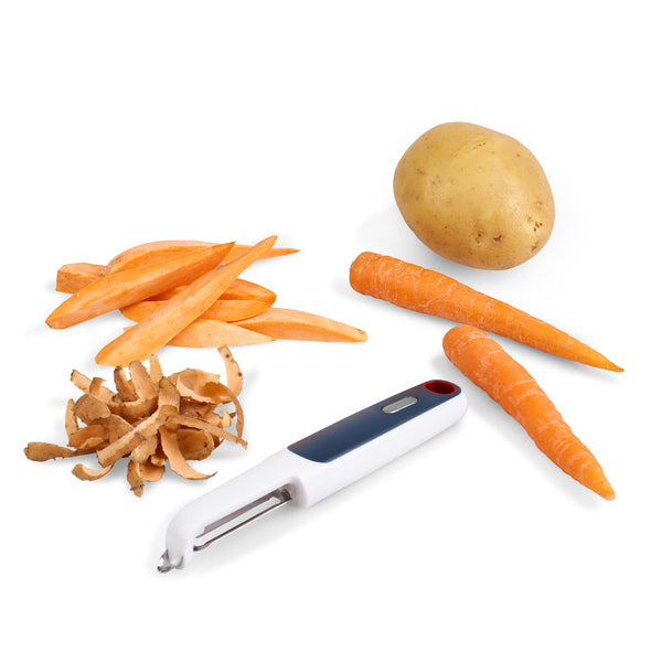 A potato, two carrots, carrot sticks, potato peels, and a Zyliss Smooth Glide Swivel Peeler with an ergonomic handle and stainless steel blades are arranged on a white surface. 