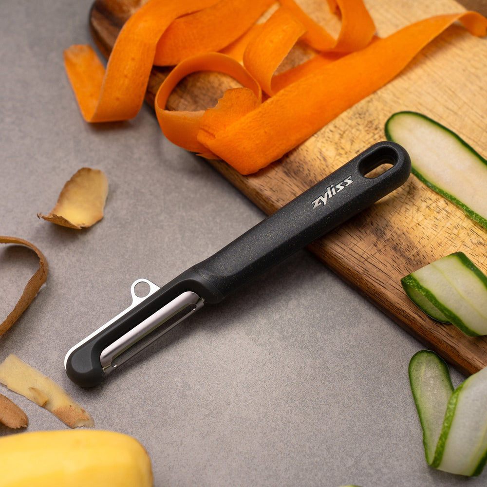 The Zyliss Swivel Peeler is black, with an ergonomic handle, straight blade, and a hole at the end. Its shown on a plain light background. 