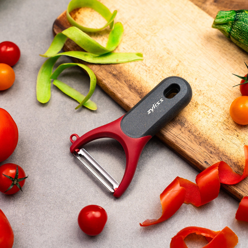 The Zyliss Soft Skin Y Peeler, shown against a white background, features a red and gray ergonomic grip, wide handle, and stainless steel blade for eco-friendly peeling. 