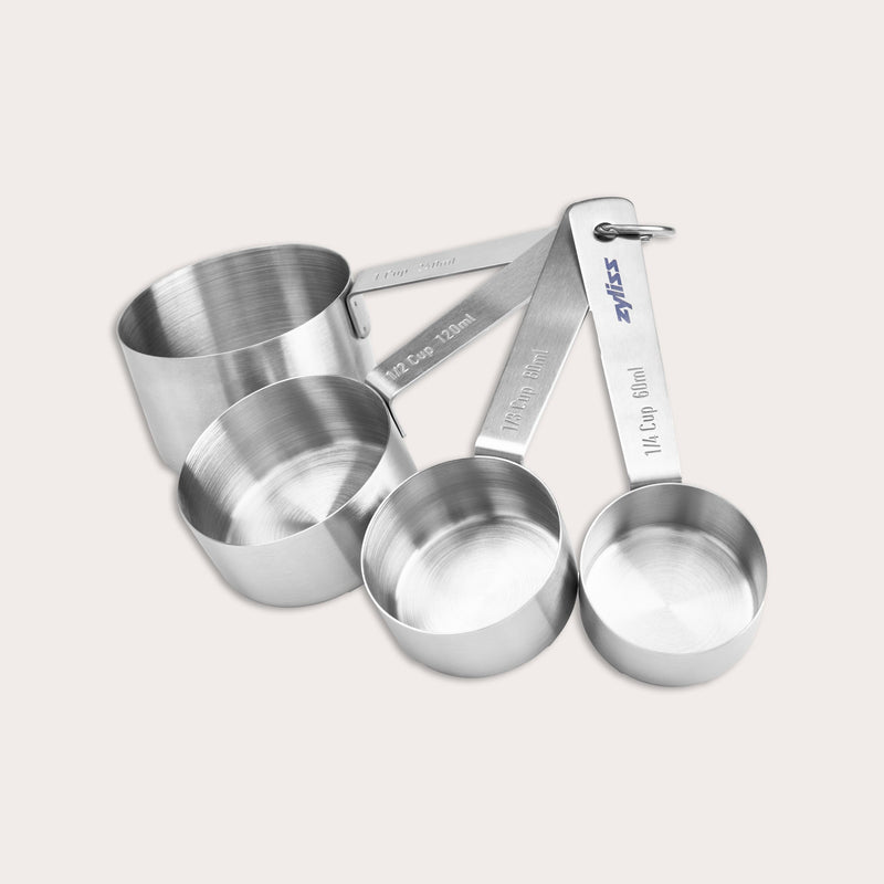 The Zyliss Stainless Steel Measuring Cups set includes four stacked, fanned-out cups, each labeled in cups and milliliters for precise ingredient measurement.