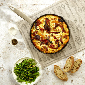 A skillet frittata with vegetables sits on a patterned cloth, served with green salad, rustic bread, and seasoning—crafted to perfection in the Zyliss Ultimate Pro Non-Stick Frying Pan With Pouring Lip for effortless release. #24cm/9½"