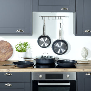 A modern kitchen with dark cabinets, wooden countertop, and pots and pans on the stove, including the Zyliss Ultimate Pro Non-Stick Saute Pan & Glass Lid. Two frying pans hang by a plant, round wooden board, and decorative artichoke. 