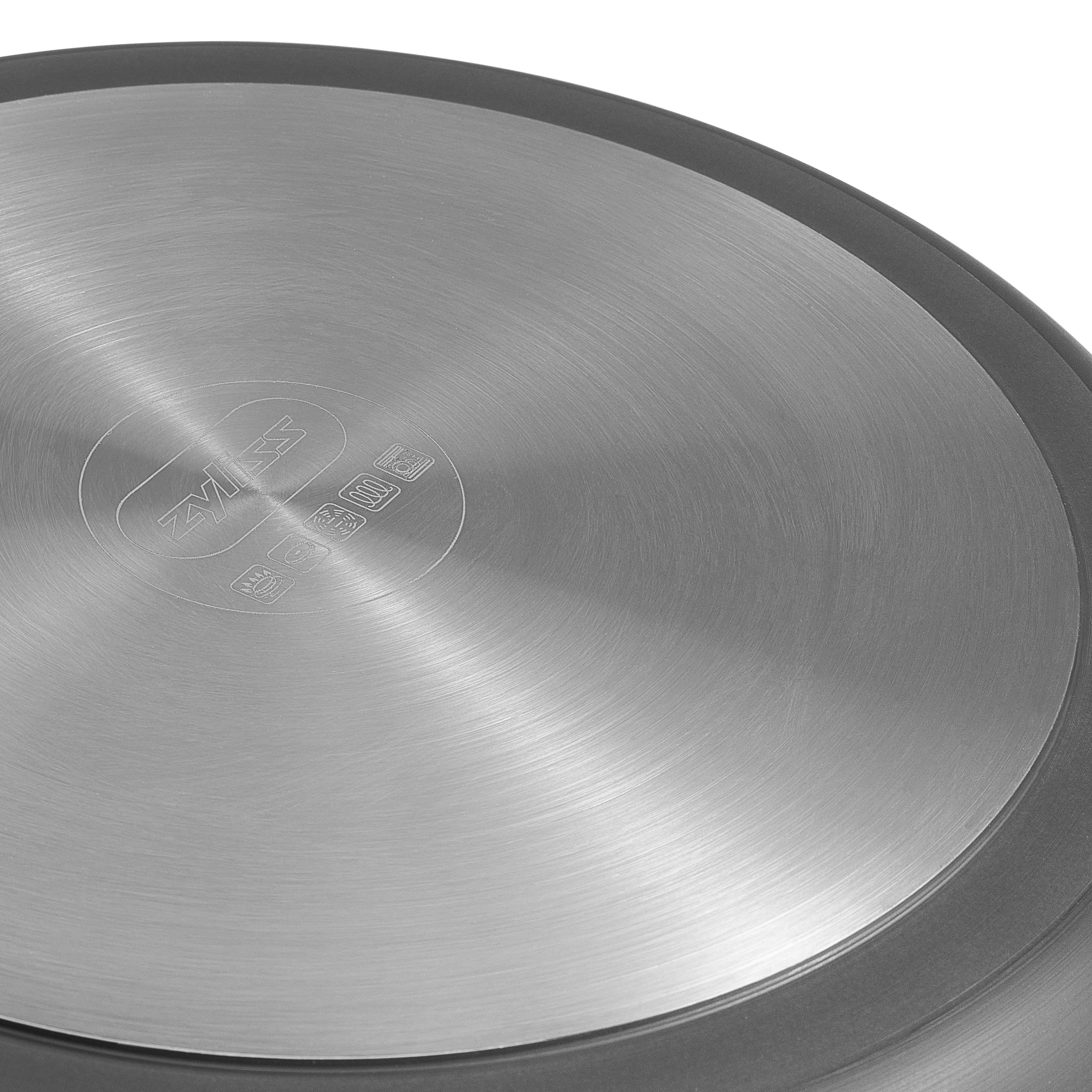 Close-up of the brushed stainless steel bottom of a cookware item, featuring engraved brand markings and symbols, with a circular, radial texture visible.