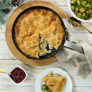 A skillet chicken pot pie with a golden, flaky crust sits on the Zyliss Ultimate Pro Non-Stick Frying Pan With Pouring Lip. A slice is served with Brussels sprouts beside bowls of cranberry sauce and more sprouts on a rustic white table. #28cm/11"