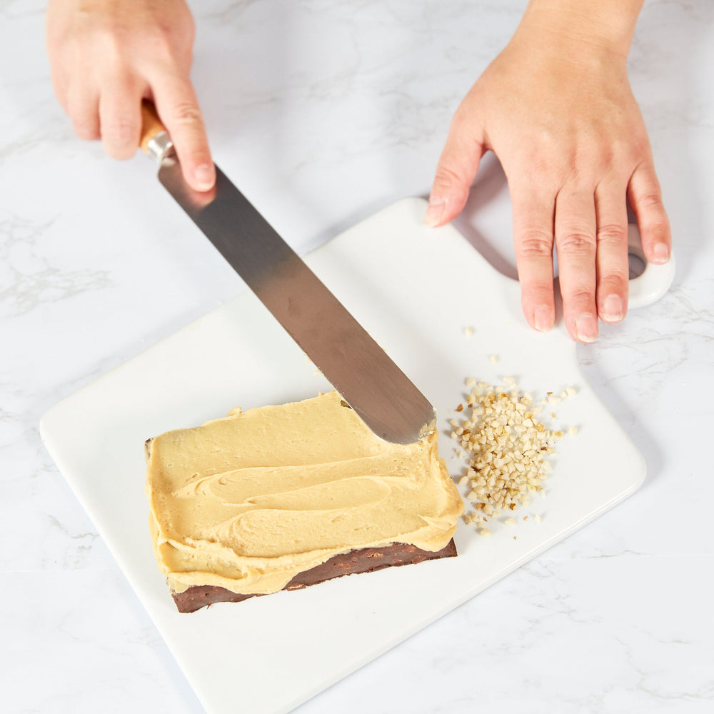 The Zyliss Beech Wood Palette Knife features an ergonomic tan beech wood handle with a dark blue tip and hanging hole, plus a long, flat stainless steel blade—ideal for spreading icing or frosting on cakes. 