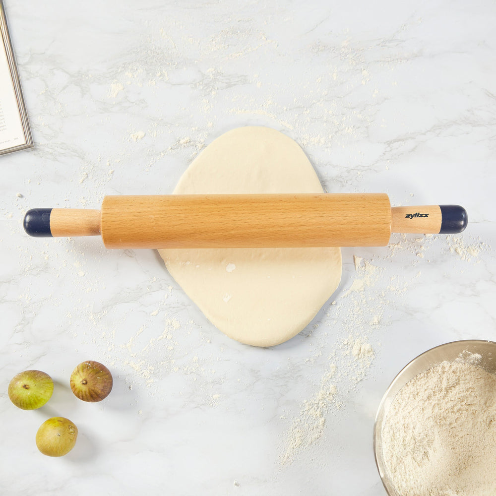 A Zyliss Beech Wood Rolling Pin with blue comfort-grip handles rests horizontally on a light background, showcasing the brand name for an essential tool in any kitchen. 
