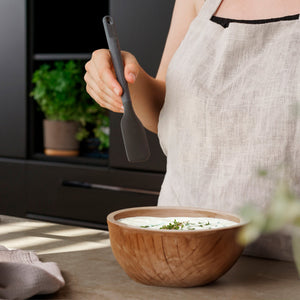 Wearing a light linen apron, a person stands by a wooden bowl of creamy mixture topped with chopped herbs, holding a Zyliss Spatula with a heat-resistant silicone head on the kitchen counter. #Small