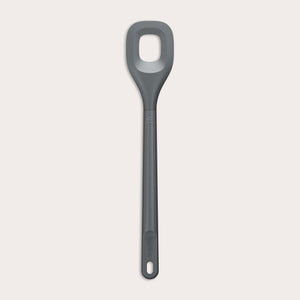 The Zyliss Square Mixing Spoon is a gray, heat-resistant silicone utensil with a long handle and a rectangular hole in the head. Shown on a plain light background, its dishwasher safe for easy cleaning. 