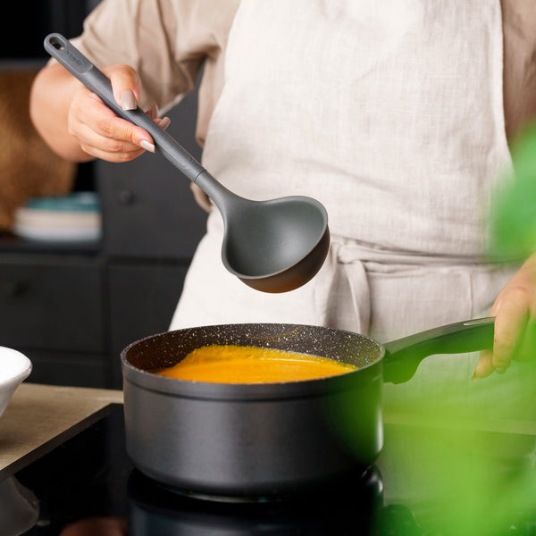 In a modern kitchen, someone in a light apron stirs orange soup on the stove using the Zyliss Ladle, showcasing the comfort of ergonomic utensils. #Large