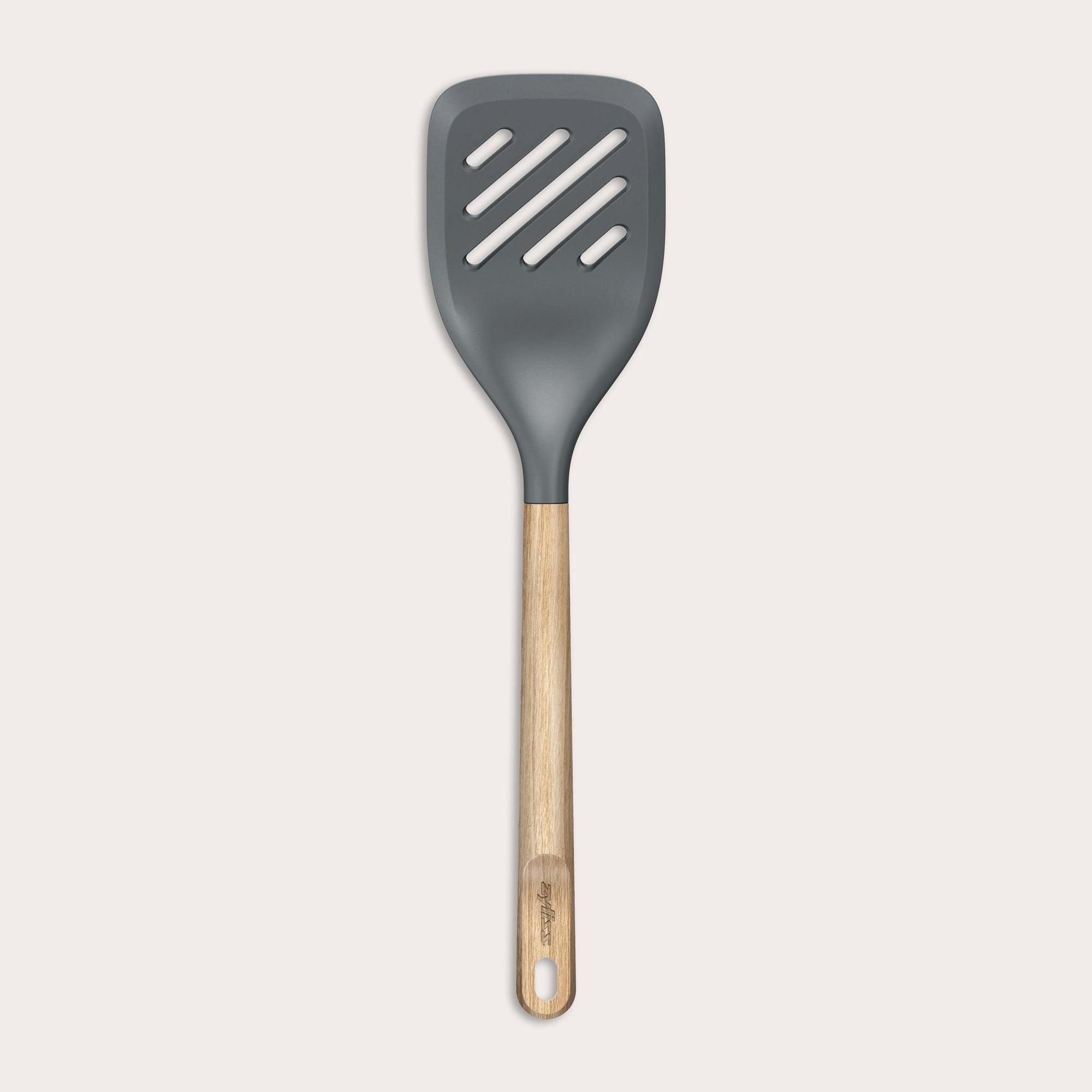 The Zyliss Oak Wood Slotted Turner is a kitchen essential with a wide, dark gray head and light oak wood handle, shown on a plain white background.