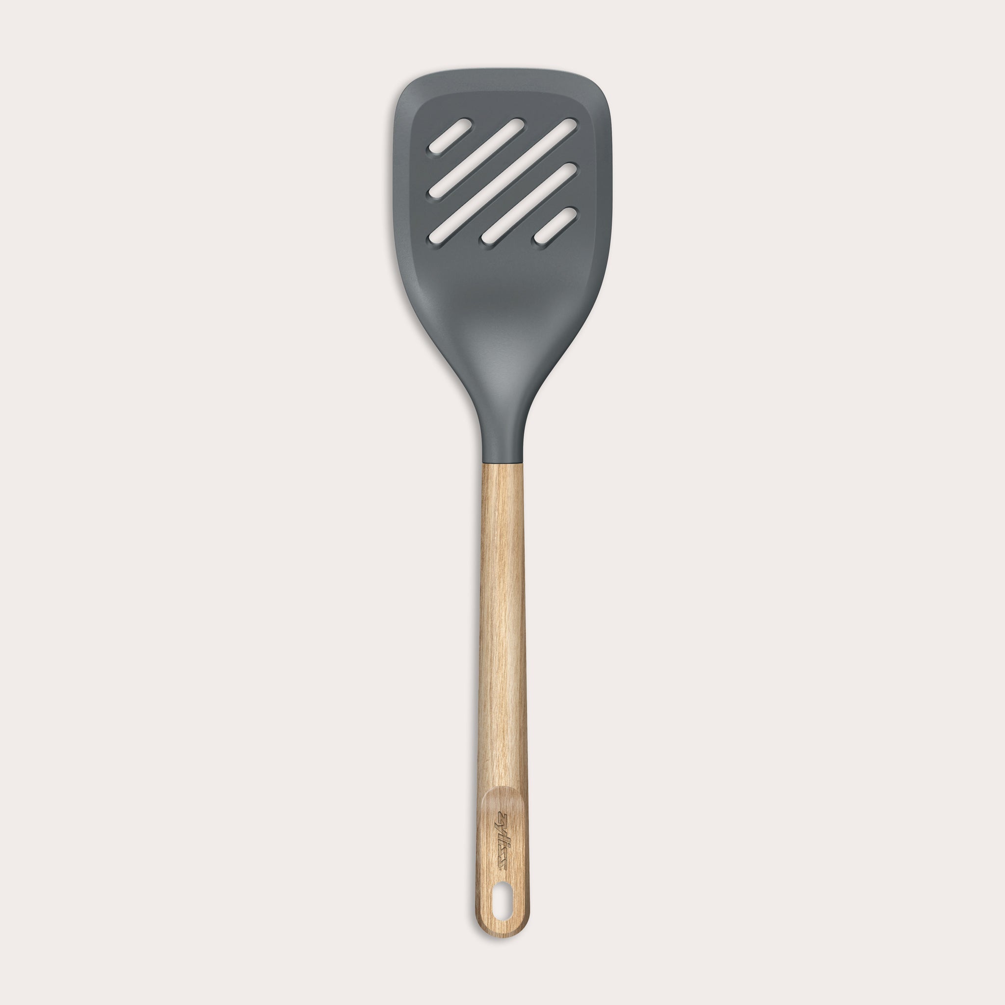 The Zyliss Oak Wood Slotted Turner is a kitchen essential with a wide, dark gray head and light oak wood handle, shown on a plain white background.
