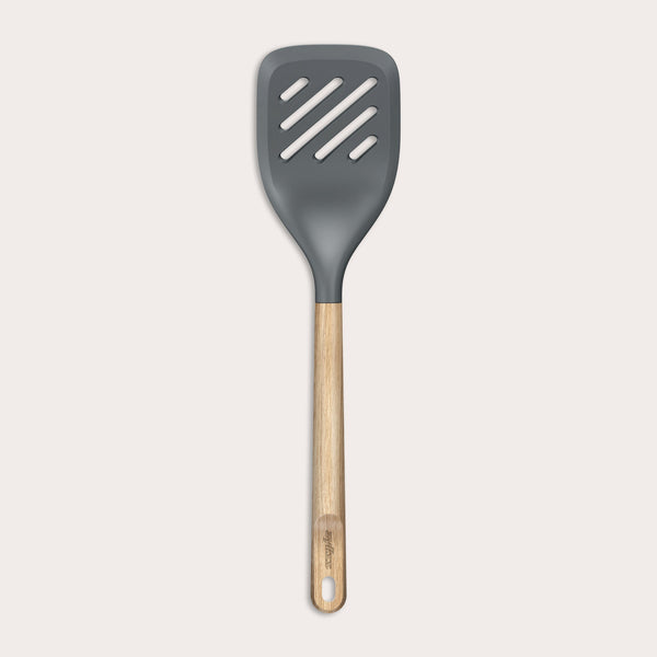 The Zyliss Oak Wood Slotted Turner is a kitchen essential with a wide, dark gray head and light oak wood handle, shown on a plain white background.