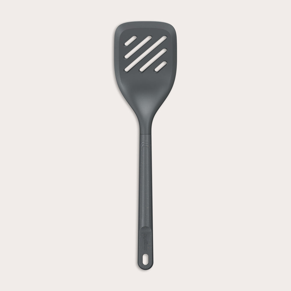 The Zyliss Slotted Turner, shown in black with three diagonal slots and an ergonomic handle, features a heat-resistant design for safe cooking or flipping food. Displayed against a plain white background. 