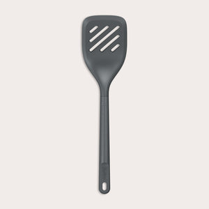 The Zyliss Slotted Turner, shown in black with three diagonal slots and an ergonomic handle, features a heat-resistant design for safe cooking or flipping food. Displayed against a plain white background. 