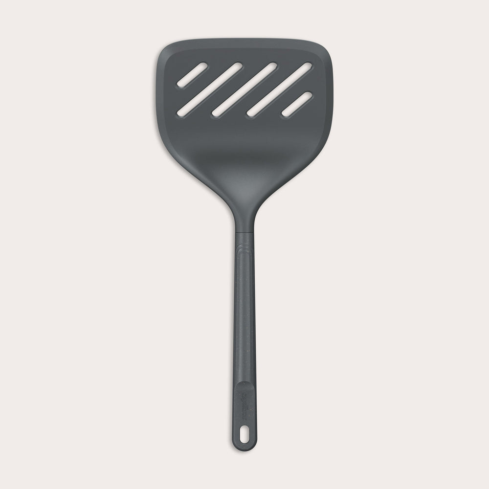 A Zyliss Turner XL slotted spatula in black, featuring a wide square head with three diagonal slots, ergonomic handle, and heat-resistant design is displayed against a plain light background. 